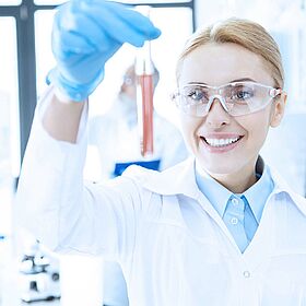 Lächelnde Chemikerin hält ein Reagenzglas mit roter Flüssigkeit in der Hand.